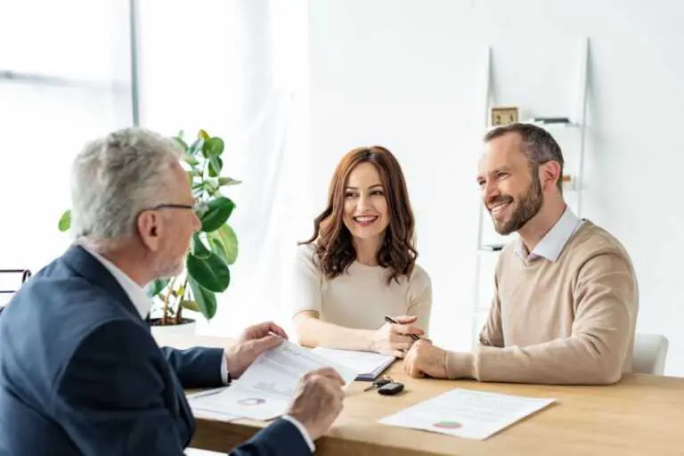 Two clients smile while discussing insurance coverage with an agent. They appear to be reviewing documents, possibly related to dental or health insurance for Invisalign in Richmond and Houston, TX.