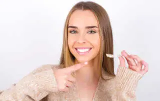 Smiling woman in Houston TX, points to her bright teeth while holding Invisalign clear aligners. Achieve a confident smile with discreet orthodontic treatment.