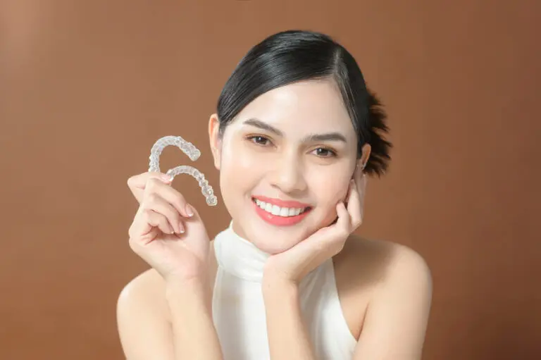 Smiling woman holds clear dental aligners, highlighting Invisalign by Elara Orthodontics in Richmond, TX.