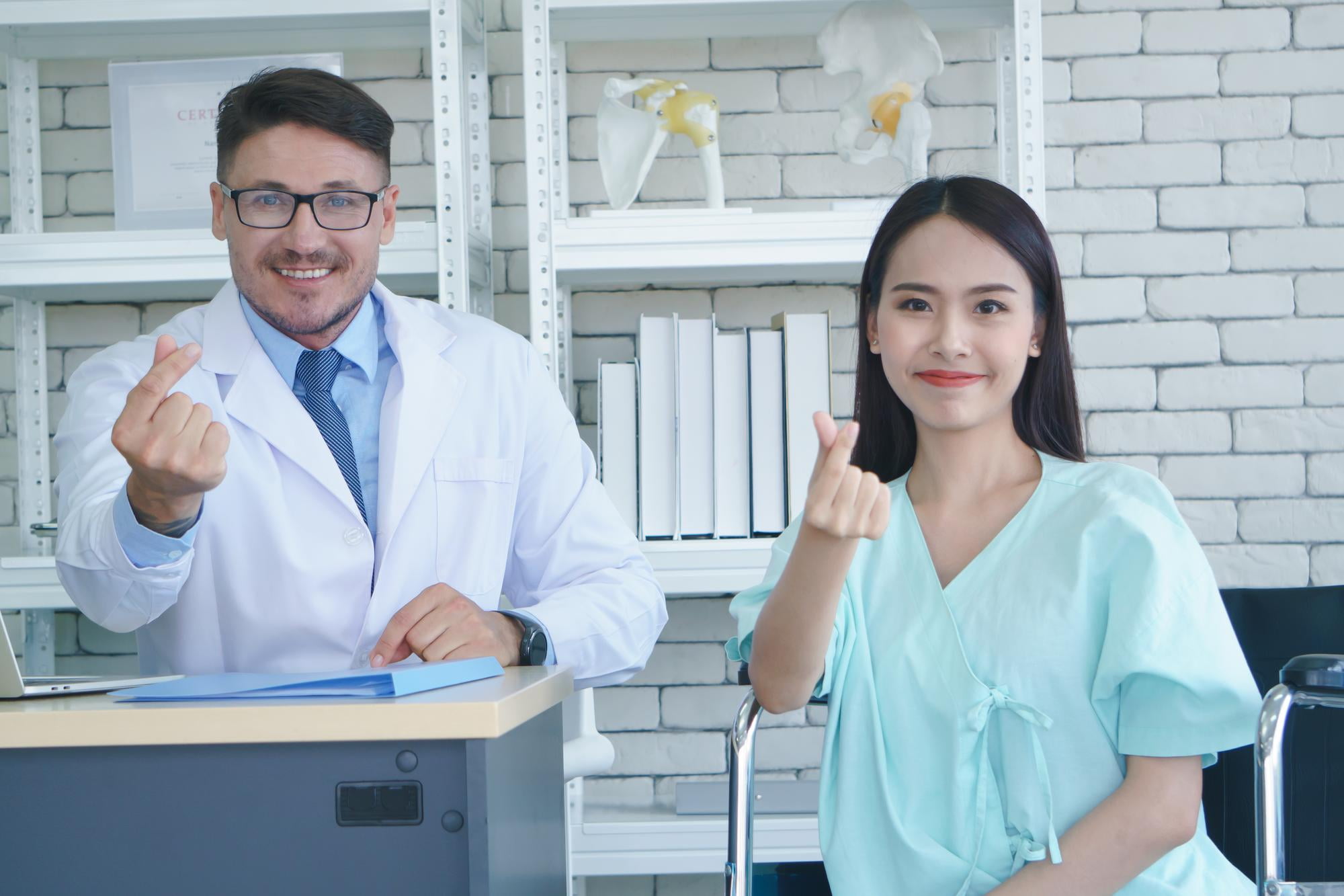 Smiling male orthodontist in white coat and female dental assistant in mint scrubs giving thumbs up in modern clinic, representing excellent patient care at Elara Orthodontics Richmond and Houston, TX.