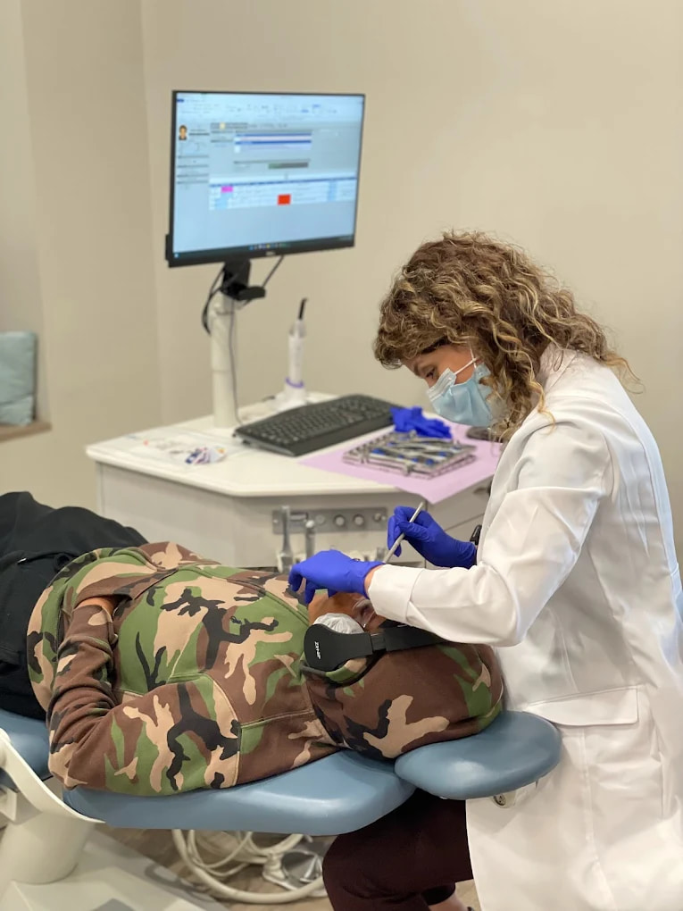 Dr. Sara Abedini and Dr. Sam Elkenawy: Orthodontist in Houston TX At Elara Orthodontics in Richmond, TX, a dentist treats a patient in camo attire; dental records show on a computer.
