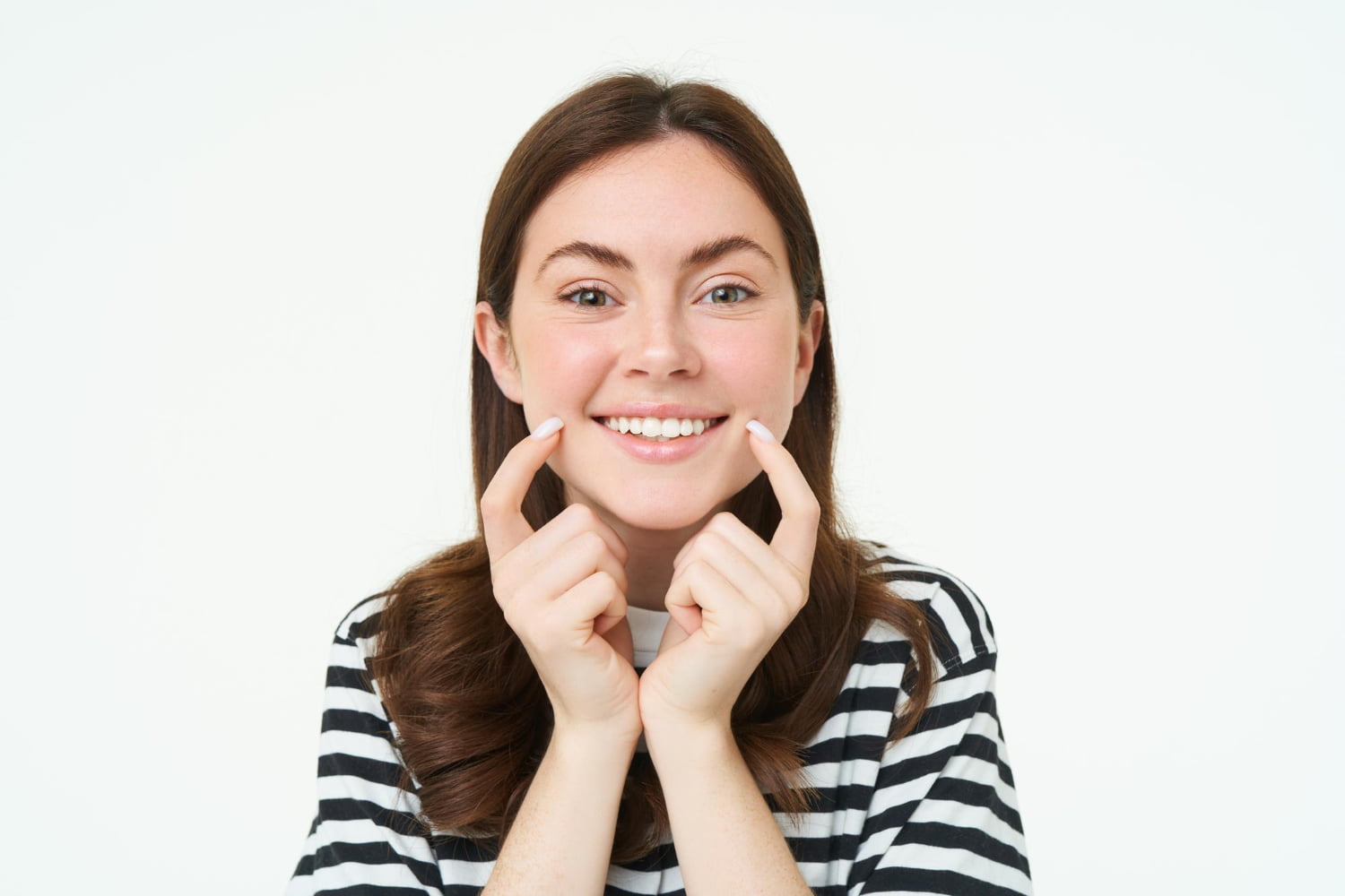 A woman in a striped shirt smiles confidently and points to her clear braces with both hands, proudly showcasing her Elara Orthodontics treatment in Richmond or Houston, TX, against a plain white background.