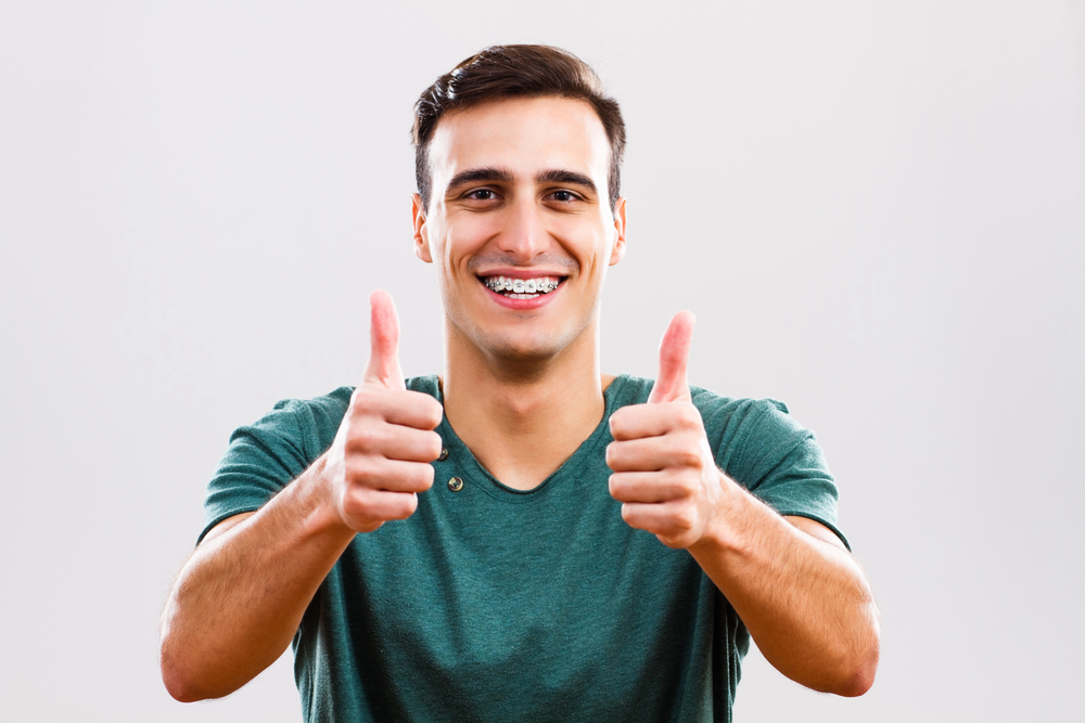 Smiling young man with braces in a green shirt gives two thumbs up for Elara Orthodontics in Houston, TX.