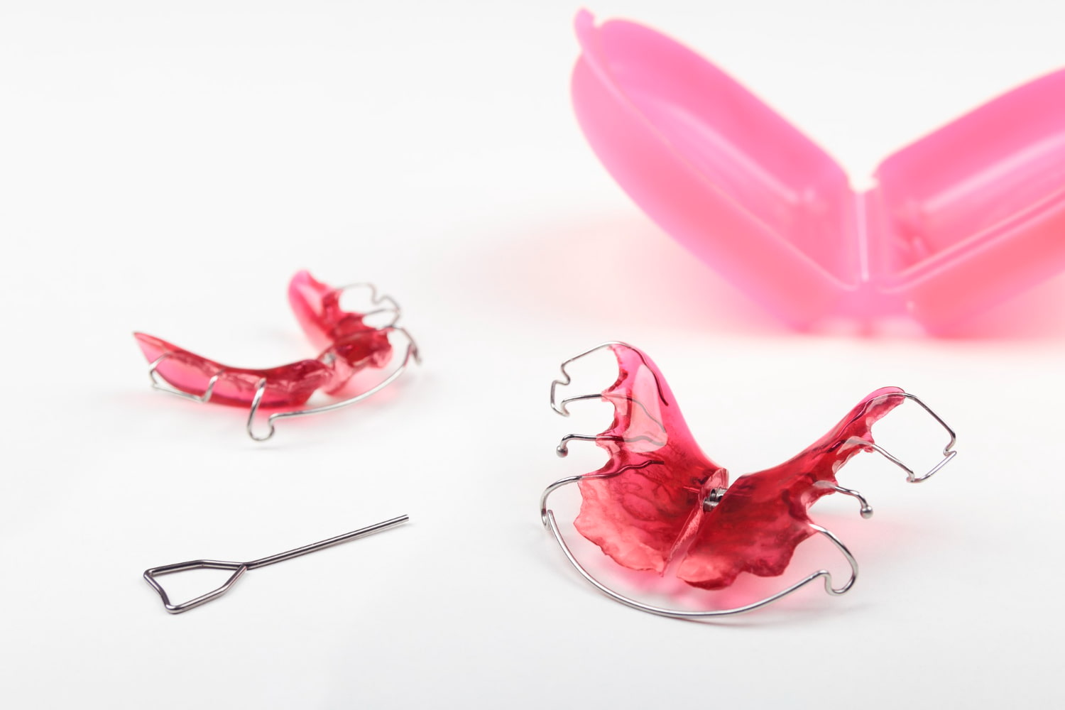 At Elara Orthodontics in Richmond or Houston, TX, children’s orthodontic essentials such as two pink retainers, a metal adjustment key, and an open pink case—part of their Functional Appliances offerings—are displayed on a white background.