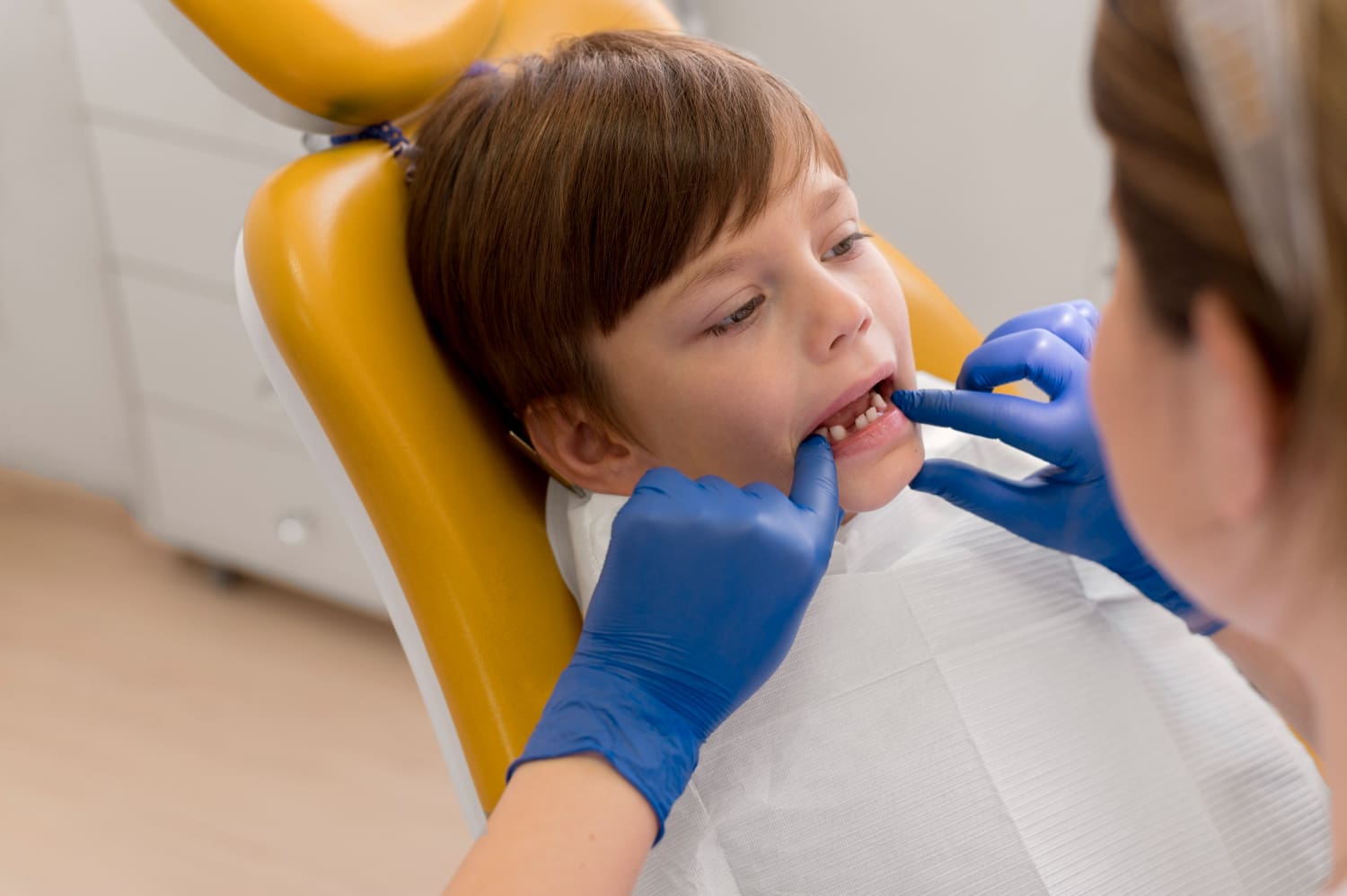 At Elara Orthodontics in Richmond or Houston, TX, a Children’s Orthodontist wearing blue gloves carefully examines a child's teeth as they sit in the dental chair.