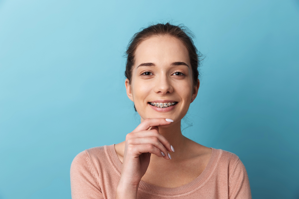 A smiling young woman with braces, possibly an orthodontic patient, poses against a blue background. Find an orthodontist in Houston, TX.