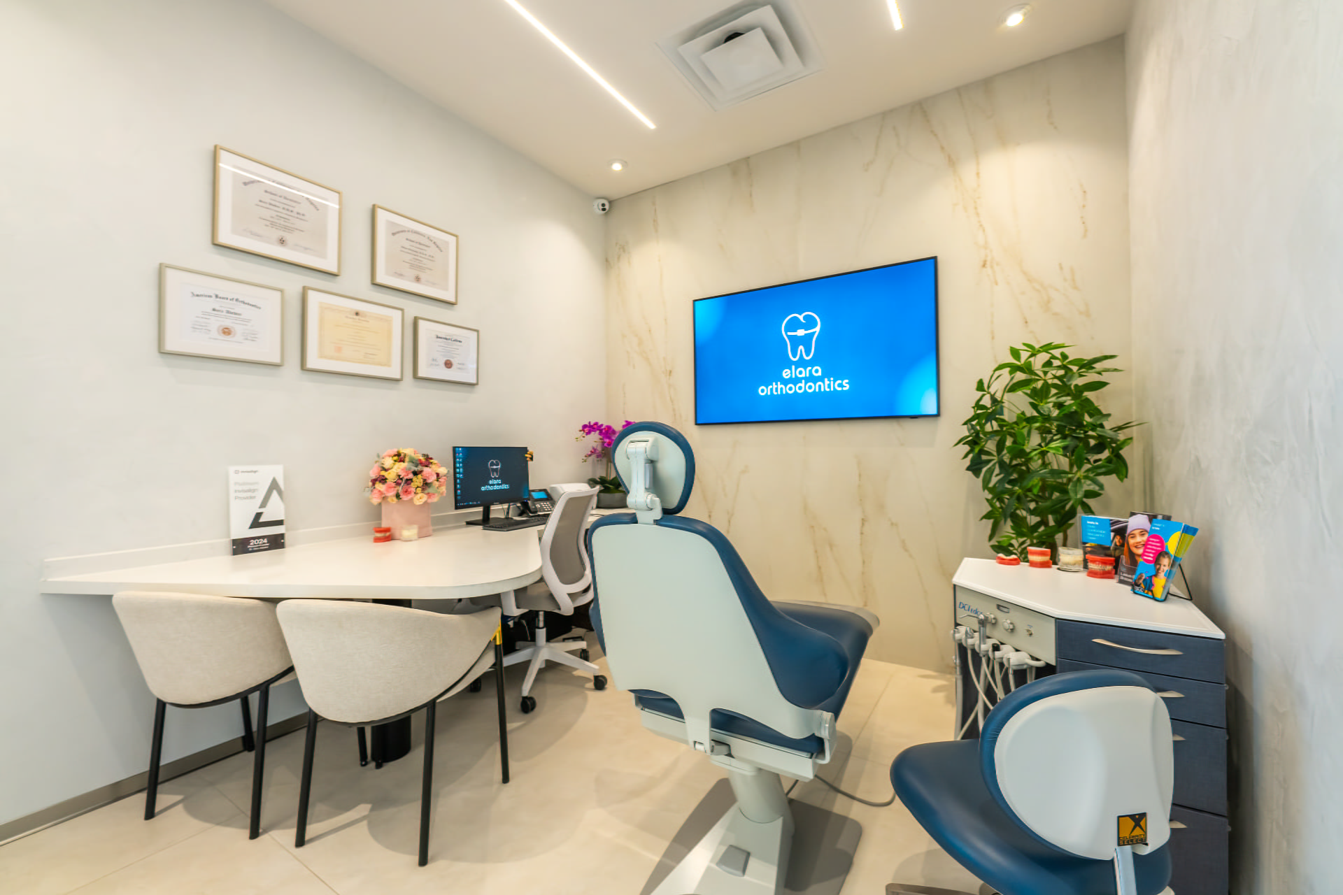 Consultation room at Elara Orthodontics in Richmond or Houston, TX with dental chair, desk, computer, certificates, and plants.