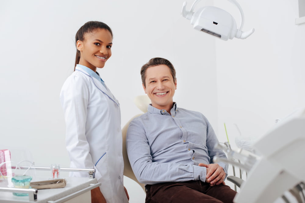 A dentist stands by a smiling male patient in a modern clinic—discover braces with Elara Orthodontics in Houston, TX.