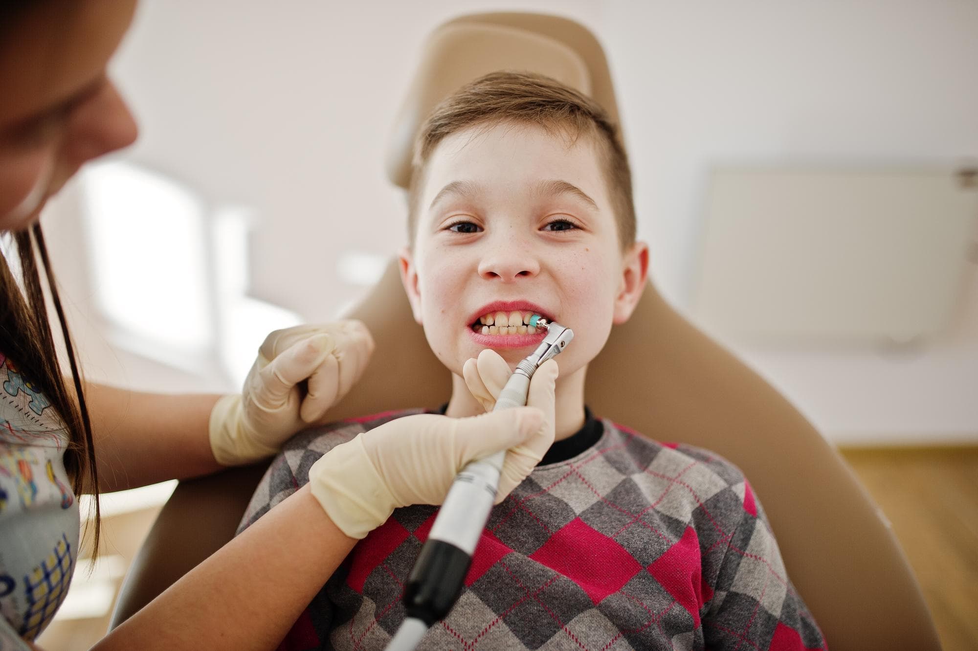 At Elara Orthodontics in Richmond or Houston, TX, a children’s orthodontist examines or cleans a child's teeth while the child sits in a dental chair.