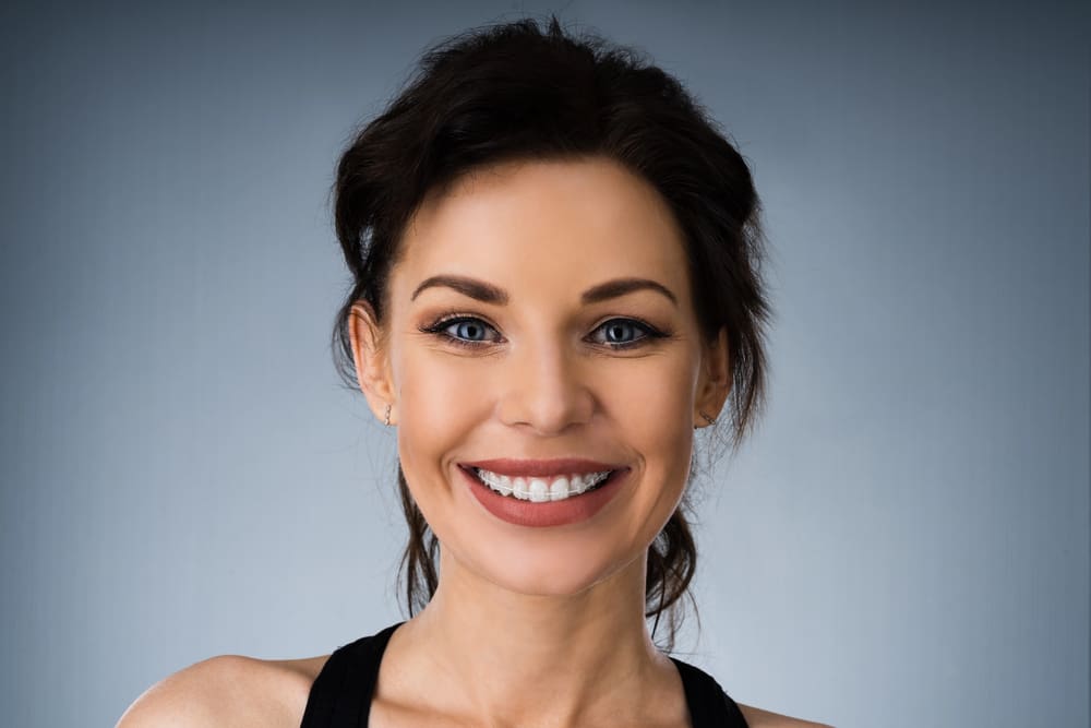 Smiling woman with dark hair and discreet Clear Ceramic Braces at Elara Orthodontics, in Richmond, TX.