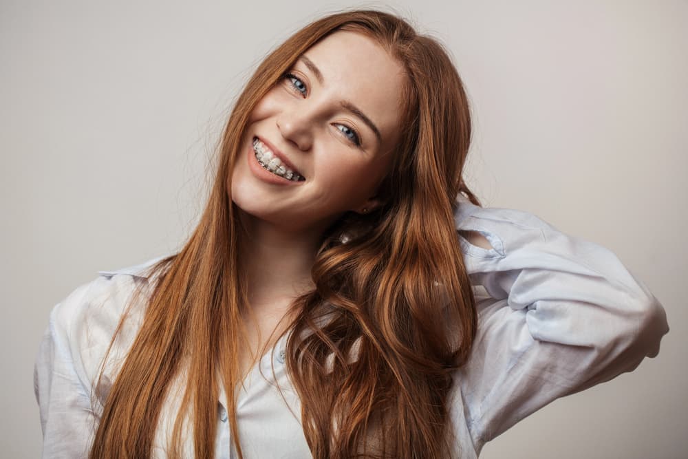 See how clear ceramic braces from Elara Orthodontics in Richmond, TX look on a smiling red-haired young woman.