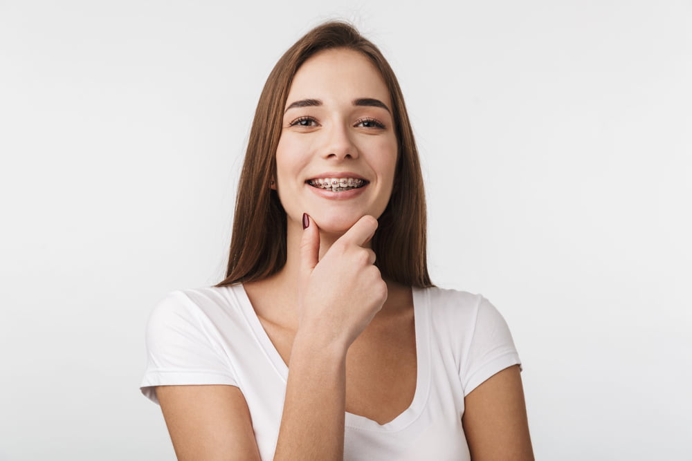 Smiling young woman with braces, in a white t-shirt, ideal for Elara Orthodontics in Richmond, TX.