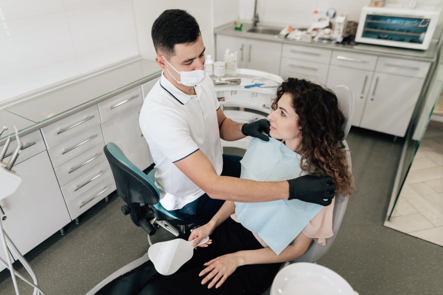 In a modern clinic, a dentist adjusts a patient's bib; Elara Orthodontics in Richmond or Houston, TX offers Palatal Expander fittings.
