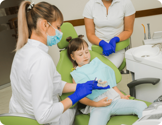 At Elara Orthodontics in Richmond or Houston, TX, a children’s orthodontist wearing gloves and a mask shows a dental mold to a young girl in the dental chair while an adult sits close by.