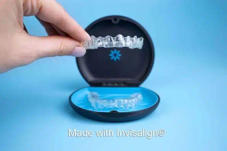 A hand holds a clear Invisalign retainer above an open black and blue case, with "Made with Invisalign®" displayed at the bottom—Elara Orthodontics offers this service in Richmond or Houston, TX.