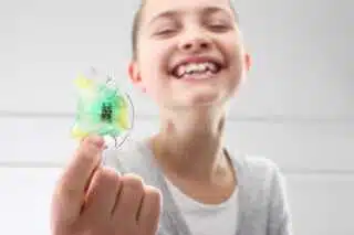 A smiling child with missing teeth proudly displays a colorful dental retainer to the camera, capturing a joyful milestone in their orthodontics treatment journey at Elara Orthodontics in Richmond or Houston, TX.