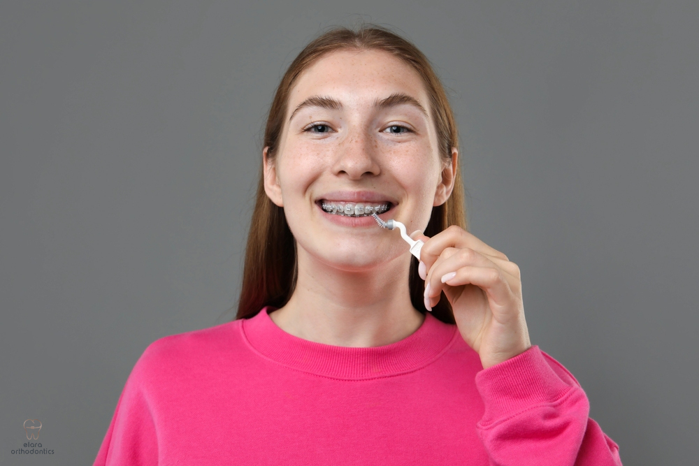 smiling girl metal braces cleaning teeth interdental brush grey background - How to Floss with Braces in Houston and Richmond, TX